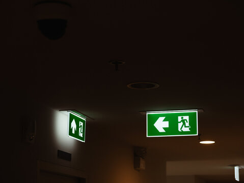 Illuminated Green Emergency Exit Direction Sign with White Right Arrow Hanging in Dark Indoor Corridor, Safety and Evacuation Concept