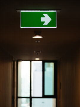 Illuminated Green Emergency Exit Direction Sign with White Right Arrow Hanging in Dark Indoor Corridor, Safety and Evacuation Concept