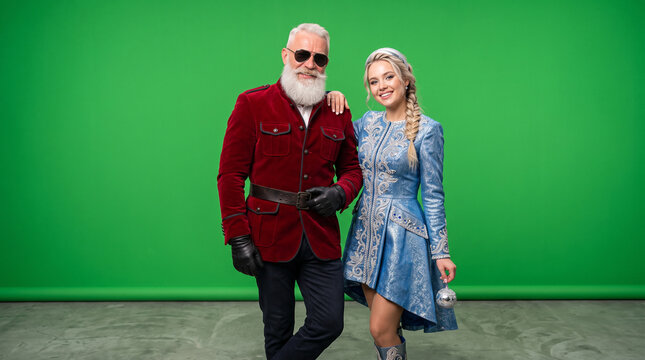 Muscular Santa Claus with a sexy young adult Snow Maiden in a festive winter outfit, bold Christmas characters posing against a green background, holiday advertising concept