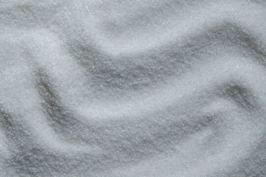White granulated sugar textured waves background closeup. Detailed full frame texture of white granulated sugar poured in abstract wavy pattern with light and shadow