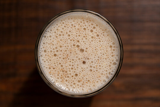 Protein smoothie or milk shake with froth in glass, closeup. Healthy protein smoothie, milkshake or plant based milk with rich foam layer in glass on dark wooden background, top view macro