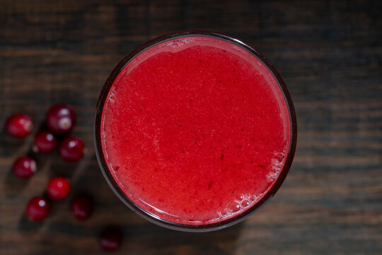 Fresh cranberry juice or smoothie in glass, closeup. Healthy red cranberry beverage or fruit smoothie in glass with fresh scattered berries on dark wooden background, top view