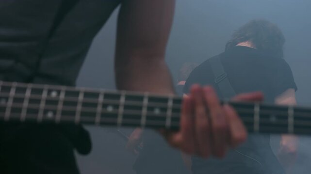 Bassist playing bass guitar closeup. Musician hands fretboard smoke stage live.