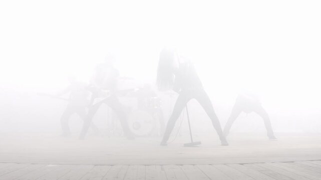 Heavy metal group performing foggy stage. Woman singer raising fist silhouette.