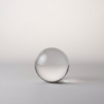 Single Transparent Glass Sphere with Subtle Light Refraction and Soft Reflections on a Neutral Surface, Minimalist Optical Object for Abstract Design and Science Concepts