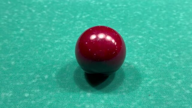 Single red billiard cue ball standing on green felt table indoors with slow zoom effect, Russian pyramid or snooker game equipment, sports hobby recreation concept.