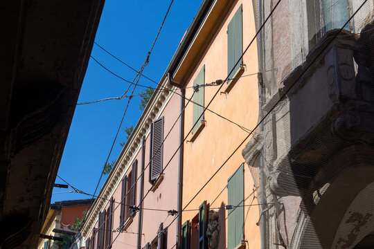 Colorful orange and pink building facades with wooden shutters under blue sky in Bologna, Italy