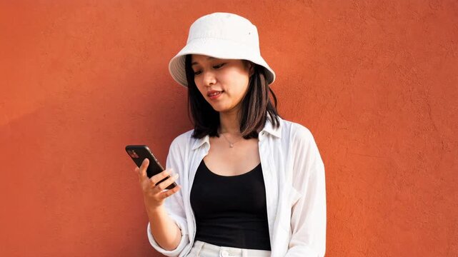 Trendy young adult asian woman using a smartphone against a terracotta wall. Sequence of frames showing a modern digital lifestyle and communication concept