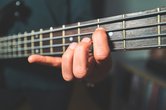 Fingers Pressing Down on Bass Guitar Strings at the Fretboard
