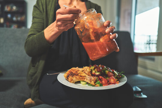 Woman Opening a Jar of Kimchi Over a Plate of Chicken and Salad