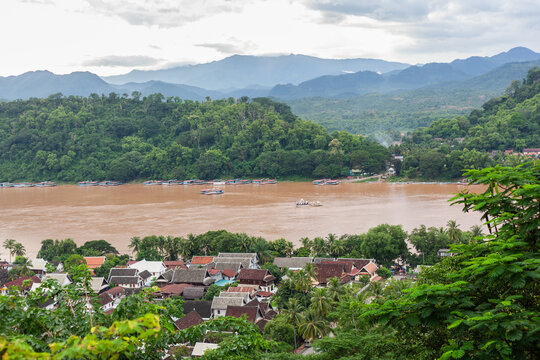 View of the Mekong River and Luang Prabang town from Phousi Hill, Laos, featuring lush green mountains and traditional rooftops under a cloudy sky.