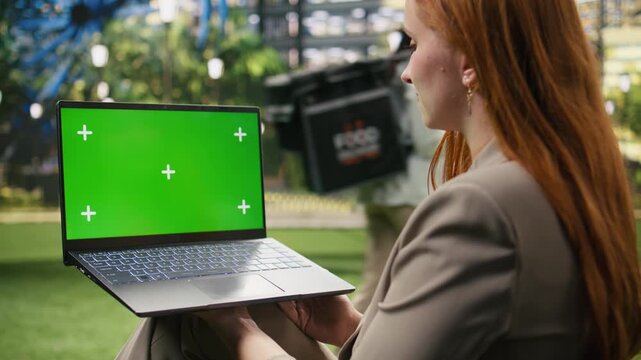 Businesswoman holds chroma key laptop in green public park