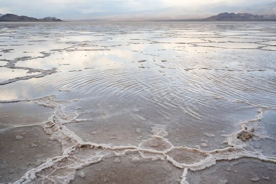 Ripples on the surface of a shallow flooded salt flat in death valley national park under a cloudy sky at sunset