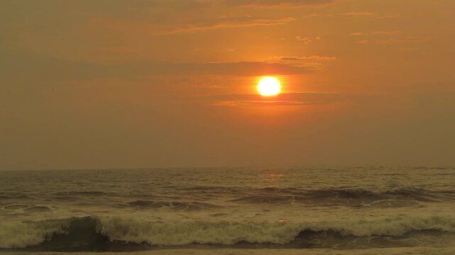 Beautiful golden sunset reflecting on wavy ocean surface with rolling sea tide under warm yellow twilight sky