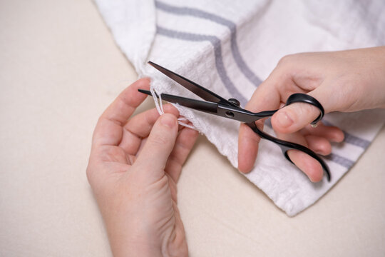 Hands cut a loose thread on a reusable white towel with scissors. DIY home textile repair, everyday household chores, housekeeping lifehacks and zero waste lifestyle.