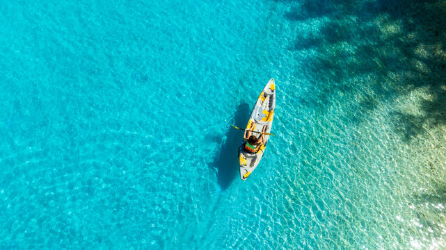 Aerial view of woman kayaking on crystal clear turquoise sea water, representing tropical travel, water sports, outdoor adventures, and relaxing vacations. concept traval	
