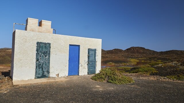 Small white building, green and blue doors, lava landscape, north, Los Lobos Island, nature reserve, blue cloudless sky, Fuerteventura, Canary Islands, Spain