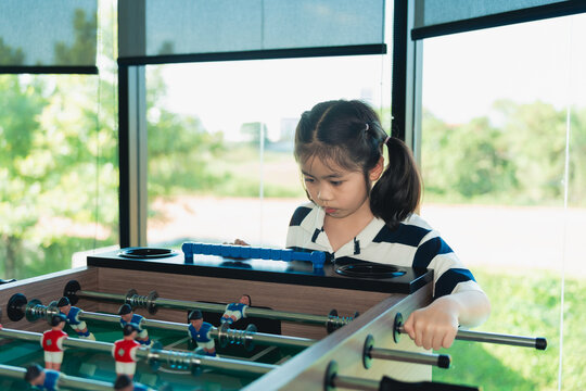 Young girl focusing intensely while playing foosball game indoors by large window with natural light