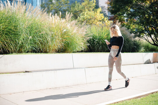 Fitness model in patterned leggings checks her phone while walking