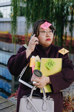 Overworked businesswoman carries work items while taking a phone call