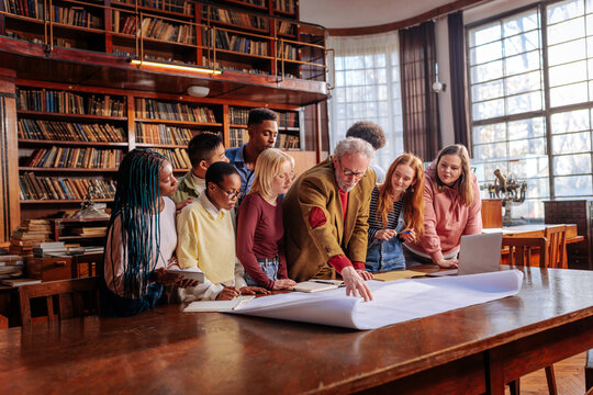 Collaborative learning session with students studying blueprints in a historic library