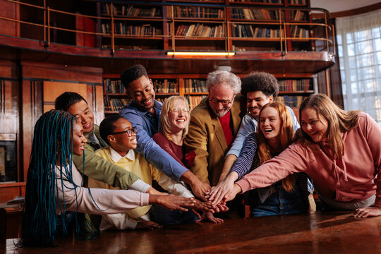 University library teamwork with student and professor stacking hands