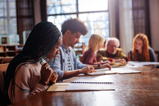 Diverse students take notes with a professor at a university library table