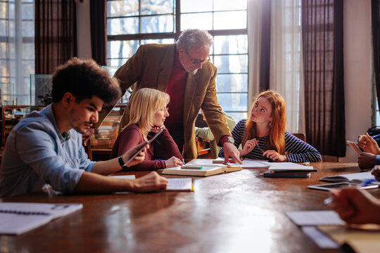 Professor teaches university students from an open book in a historic library