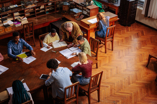Students read with a professor while researching at a library table