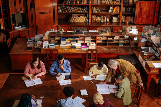 University students study with professor around a table in historic library
