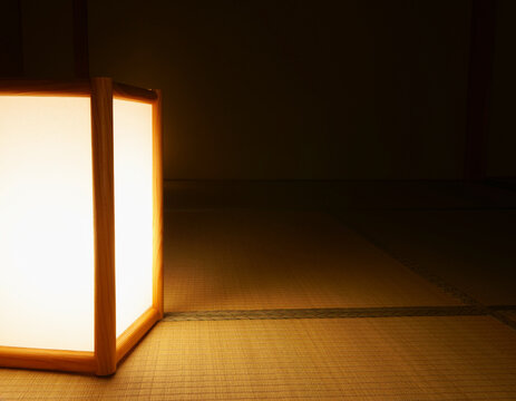 Glowing paper andon lamp with a wooden frame on tatami mats in a dark Japanese room