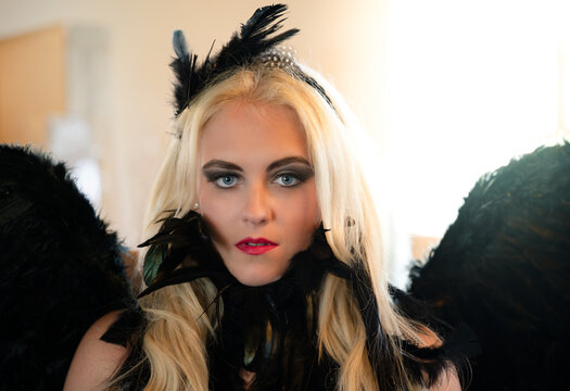 Beautiful blonde woman dressed as dark angel with black feather wings and dramatic makeup