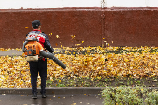 Worker with leaf blower clears away autumn leaves