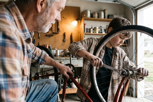 Senior grandfather and young grandson repairing an old bicycle together in a home garage workshop, boy using a wrench to tighten the wheel axle nut