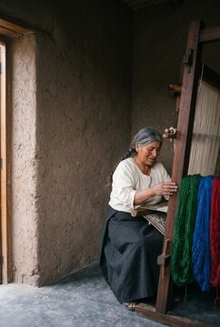 Senior Indigenous Artisan Woman Weaving Traditional Textile on Wooden Loom in Rustic Adobe Room with Colorful Yarn