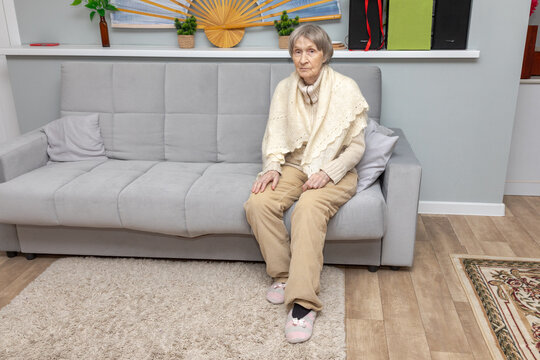 Elderly grandmother sitting alone on sofa in living room. Senior woman at home. Aging, retirement and later life. Domestic comfort and independent living