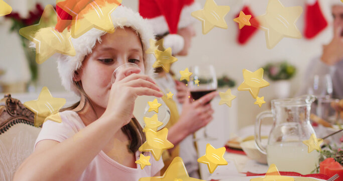 Image of stars falling over happy caucasian family wearing santa hats and having dinner