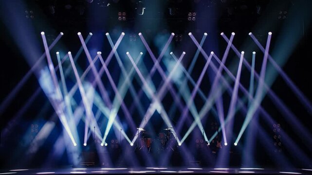 Beams of white and violet stage light crossing through haze above a dark concert set