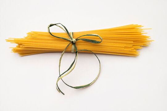Uncooked spaghetti on light gray background highlights wheat pasta texture and warm golden color, offering versatile imagery for Italian cuisine marketing, recipe publications and culinary