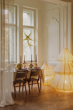 Elegant and cozy dining room decorated for Christmas with festive table setting, glowing paper tree lamps, candles, and warm festive ambiance