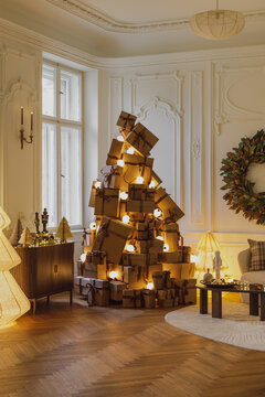 Creative Christmas tree made of wrapped gift boxes in elegant classic living room interior with festive lights, wreath, and holiday decor