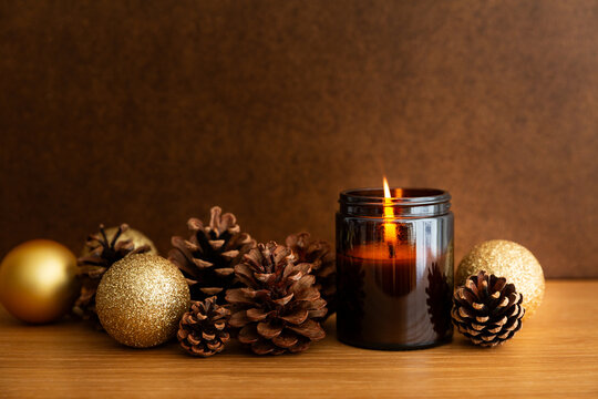 Bougie allum&eacute;e dans un pot en verre ambr&eacute; avec pommes de pin et boules de No&euml;l paillet&eacute;es et dor&eacute;es sur une table en bois, ambiance douce et chaleureuse