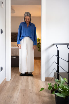 Mature woman standing on a scale at home checking her weight