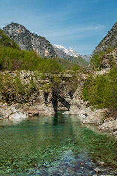 Wooden suspension bridge over clear turquoise river in Theth Albania
