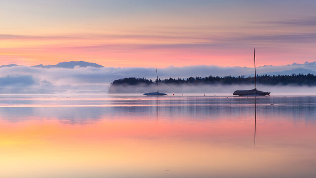 Sailboats on Lake Starnberg at sunrise with morning fog and mountains