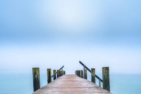 Wooden Jetty extending into foggy Lake Starnberg in autumn morning