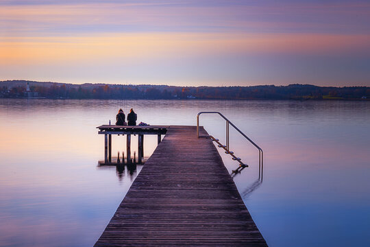 Two women sitting on a jetty overlooking Lake Starnberg at sunset
