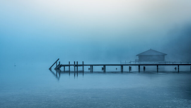 Boathouse with wooden jetty on foggy Lake Starnberg in Bavaria Germany