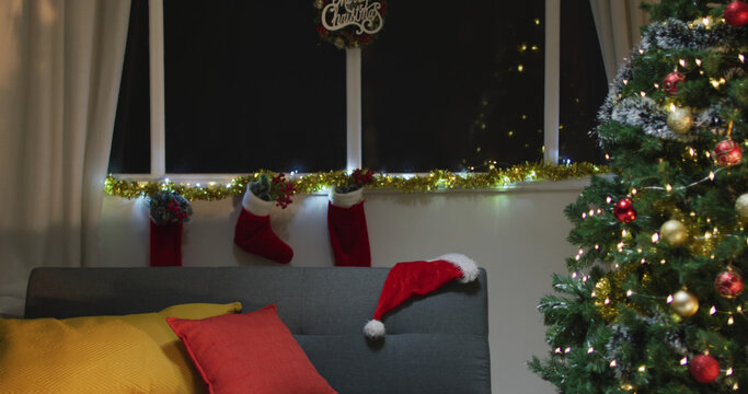 Image of christmas greetings, decorations, christmas tree, lights and christmas stockings at home