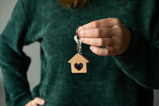 Buying or renting real estate. New homeowner holds up her keys against a gray wall, celebrating a move to a new home